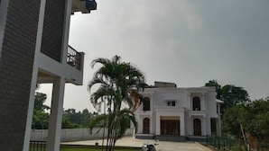A building with a balcony, a motorcycle, and a palm tree. - Rani Kutir Resort (Bolpur)