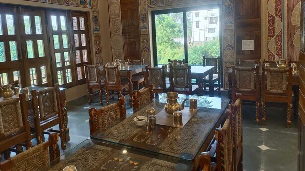 A traditional dining area with wooden furniture and patterned wall decorations. - Rani Kutir Resort (Bolpur)
