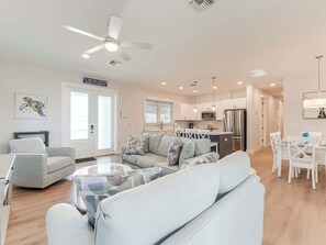 A modern apartment with a living room, dining area, kitchen, and a ceiling fan.
