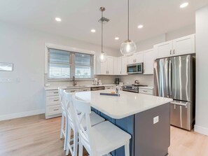 A modern kitchen with white cabinetry, stainless steel appliances, a central island with bar stools, and pendant lighting.