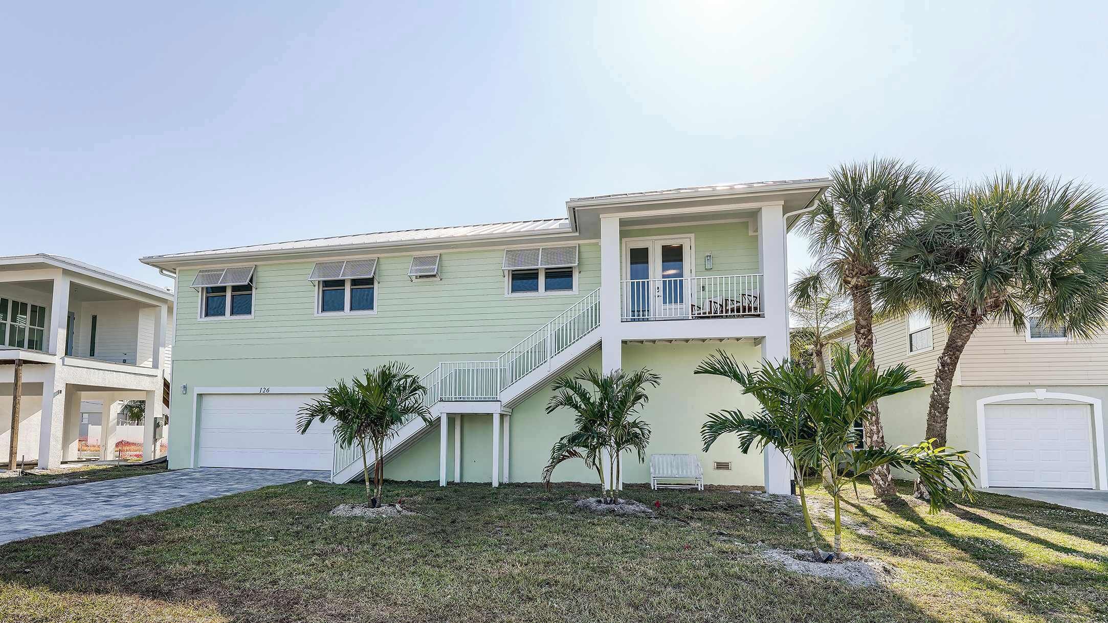 A two-story house with a covered front porch, a staircase leading to the upper floor, and a small front yard with palm trees.