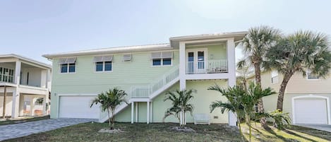 A two-story house with a covered front porch, a staircase leading to the upper floor, and a small front yard with palm trees.