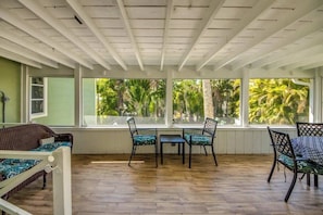 A room with a wooden floor, a white ceiling, and large windows with a view of palm trees.