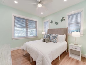 A bedroom with a bed, two bedside tables, a ceiling fan, and two windows with blinds. - 126 Gulf Island Peaceful Pool Home near Beach (Fort Myers Beach)