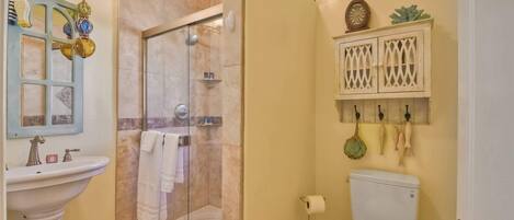 Un baño con cabina de ducha de vidrio, lavabo con espejo e inodoro.
