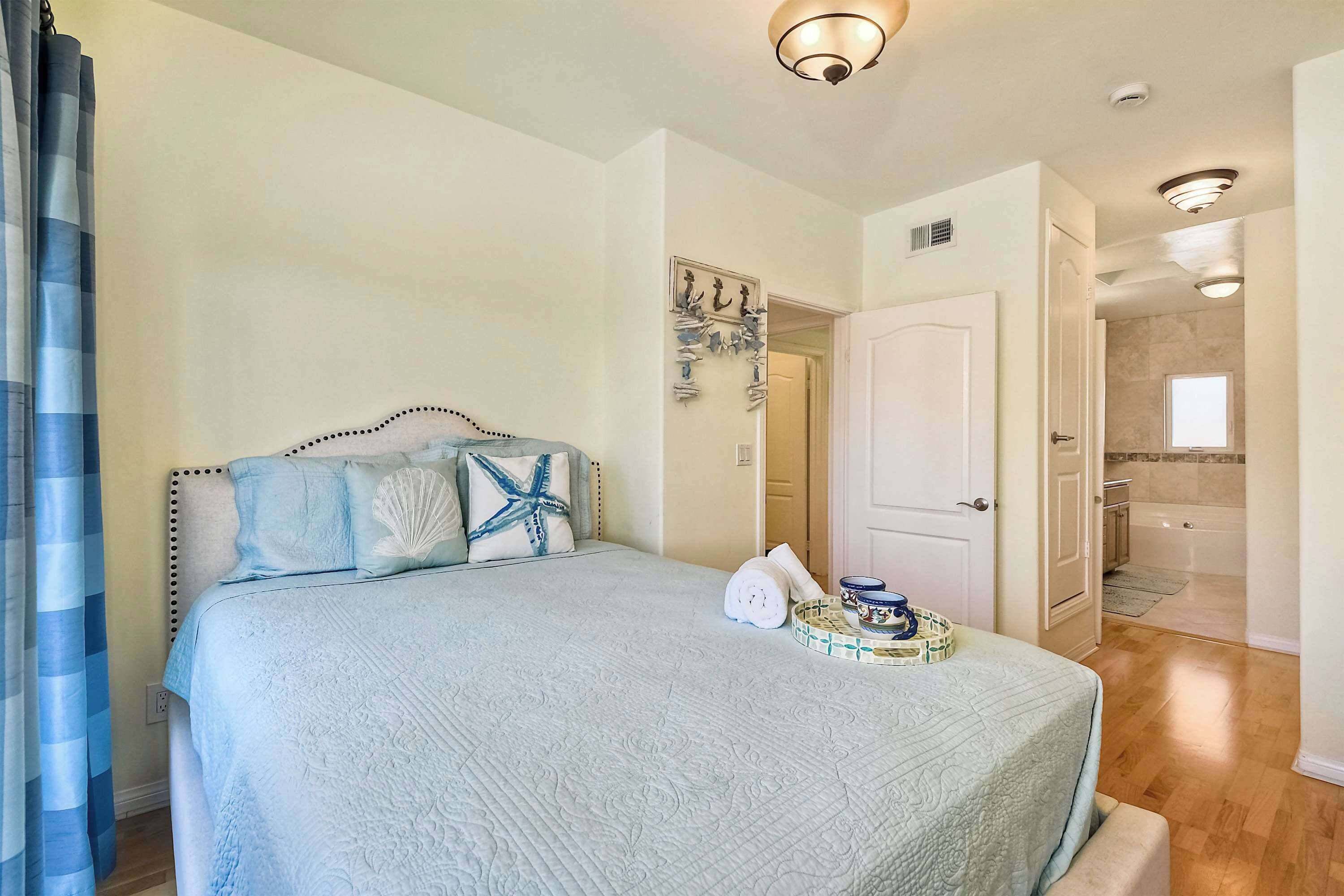 A bedroom with a bed, a nightstand, a wall clock, and a door leading to a bathroom.