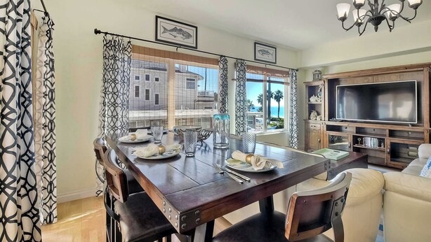 A dining area with a wooden table set for four, a TV, and a view of a building through the window. - South Pacific Walk to Beach! (Oceanside)