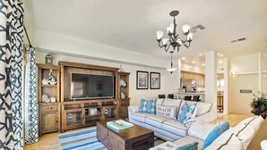 A modern living room with a large flat-screen TV, wooden entertainment unit, and a sofa with decorative pillows. - South Pacific Walk to Beach! (Oceanside)