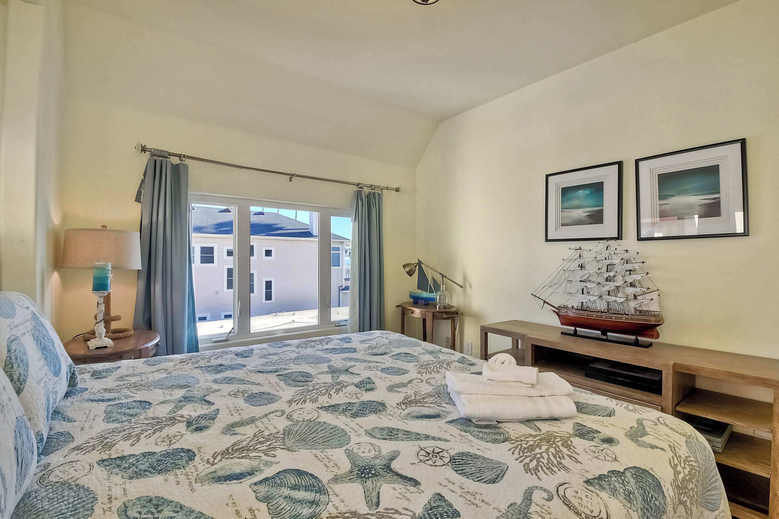 Habitación de hotel con cama, escritorio, modelo de barco y dos cuadros en la pared.