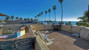 A rooftop terrace with a view of the ocean, palm trees, and outdoor seating. - South Pacific Walk to Beach! (Oceanside)