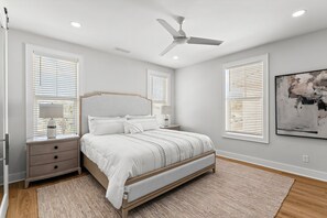 A bedroom with a bed, nightstands, a ceiling fan, and large windows with blinds.