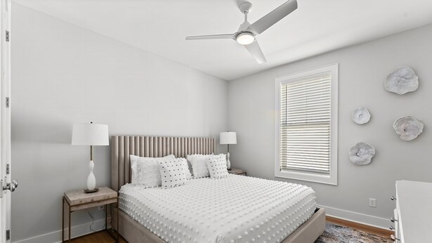 Un dormitorio con cama, mesitas de noche, ventilador de techo, ventana con persianas y decoración en la pared.