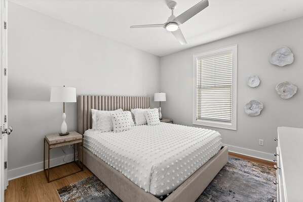 Un dormitorio con cama, mesitas de noche, ventilador de techo, ventana con persianas y decoración en la pared.
