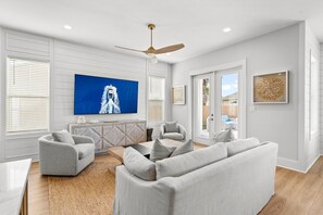 A modern living room with a large flat-screen TV, a ceiling fan, and a sliding glass door leading to a patio.
