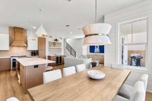 A modern kitchen with a central island, pendant lighting, and a dining area with a wooden table and chairs.