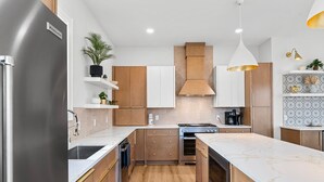 Cocina moderna con refrigerador de acero inoxidable, armarios de madera, una isla central y una lámpara colgante.
