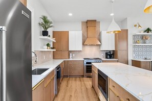 Cocina moderna con refrigerador de acero inoxidable, armarios de madera, una isla central y una lámpara colgante.