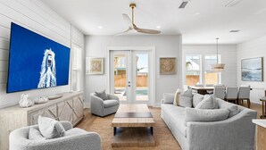 Una sala de estar moderna con un televisor de pantalla plana, un ventilador de techo y una zona de comedor con una mesa y sillas.