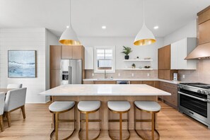 Une cuisine moderne dotée d’un îlot central, de tabourets de bar, d’un four encastré et de luminaires suspendus.