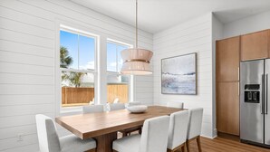 Una cocina moderna con una mesa de comedor de madera, sillas blancas, un refrigerador de acero inoxidable y una lámpara colgante.