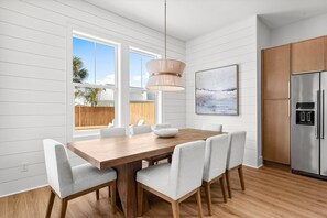 Una cocina moderna con una mesa de comedor de madera, sillas blancas, un refrigerador de acero inoxidable y una lámpara colgante.