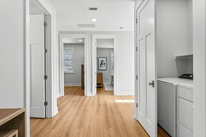 Un couloir avec des portes blanches, un plancher en bois et un coin buanderie équipé d’un lave-linge.