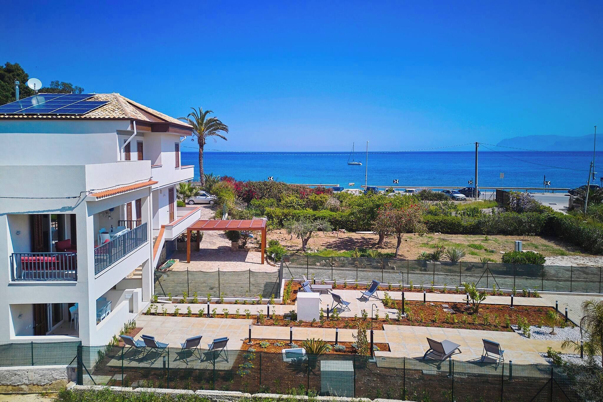 Um edifício moderno com painel solar no terraço, área de piscina com espreguiçadeiras e vista para o mar.