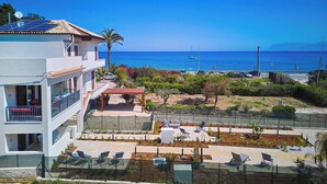 Un edificio moderno con paneles solares en la azotea, un área de piscina con sillas de descanso y vistas al mar.