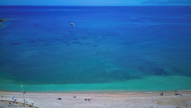 Una playa con agua turquesa cristalina, un bote pequeño y gente relajándose en la orilla.