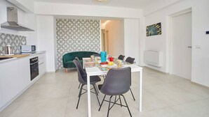 Una cocina moderna con armarios blancos, horno empotrado y comedor con mesa blanca y sillas negras.