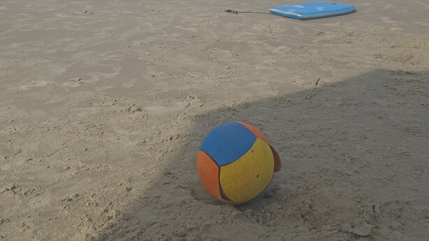 Una playa con una red de voleibol y una tabla de surf azul sobre la arena.