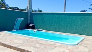Una piscina con un borde empinado con baldosas, una sombrilla roja y una pared verde al fondo.