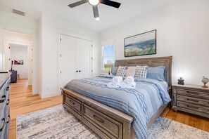 A bedroom with a bed, a nightstand, a dresser, a ceiling fan, and a painting on the wall.