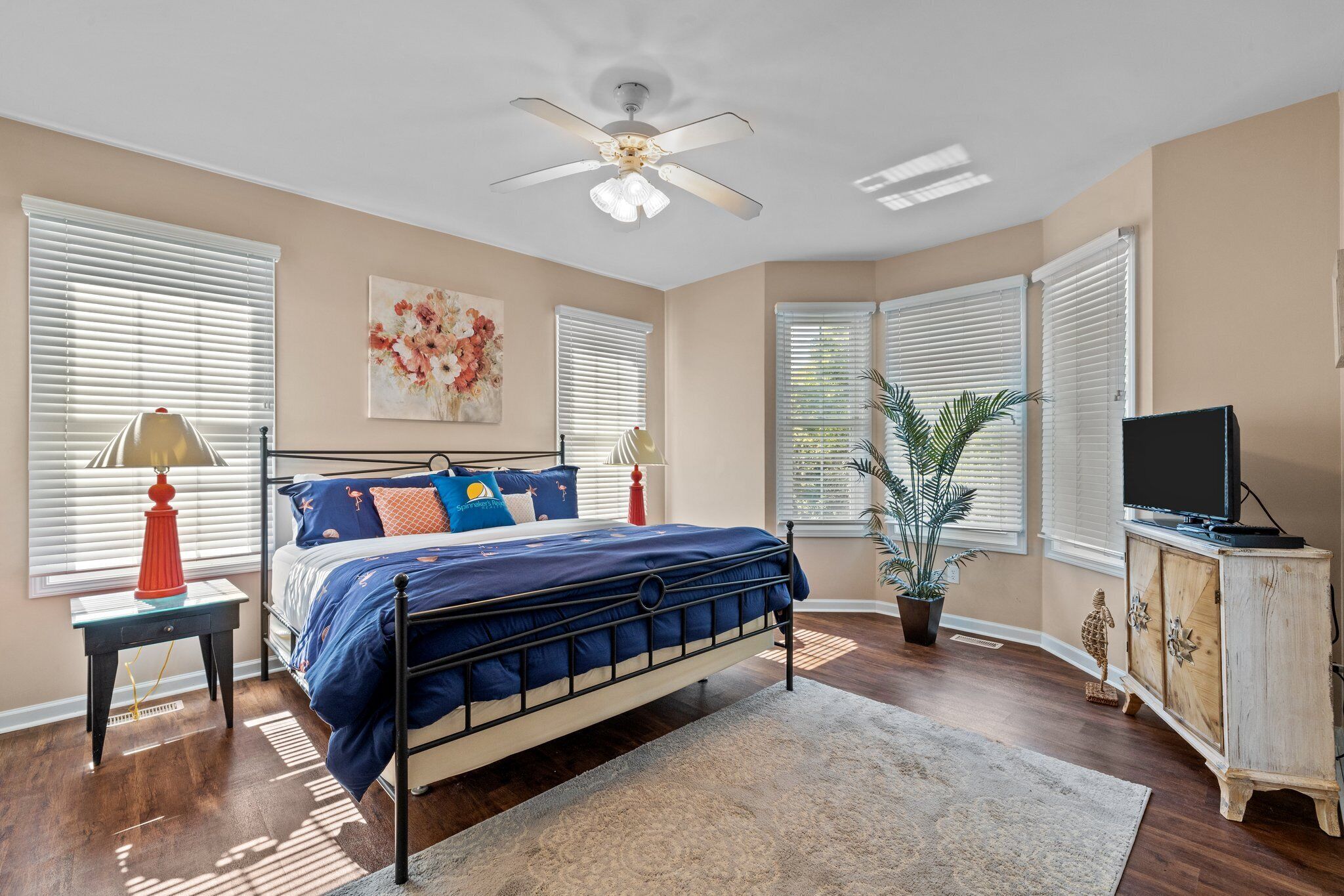 A bedroom with a bed, a ceiling fan, a TV, and a potted plant.