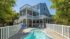 A two-story house with a swimming pool, white railings, and outdoor seating.