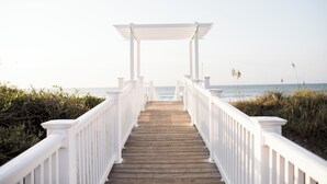 A wooden pathway leading to a white pergola with a view of the ocean.