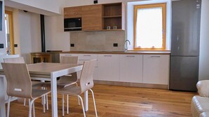 Een moderne keuken met houten kastjes, een roestvrijstalen koelkast, een inbouwoven en een raam dat natuurlijk licht binnenlaat.