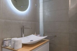 Een moderne badkamer met een witte wastafel, een spiegel en een houten aanrecht.