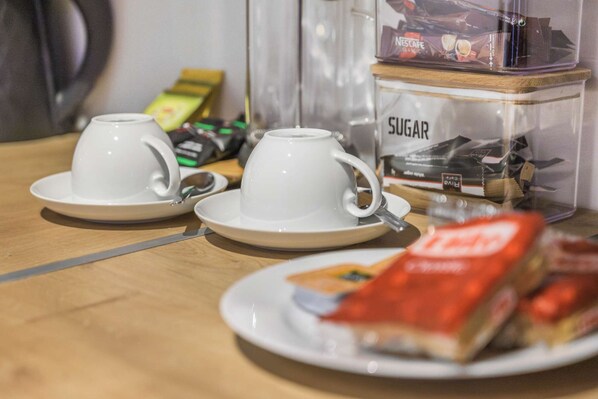 Two white cups on saucers, a packet of sugar, and a packet of tea on a wooden table.