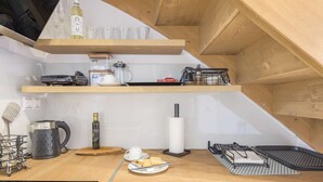 Een compacte keuken met houten planken, een koffieapparaat, een waterkoker en een klein eethoekje met een schaal brood en boter.