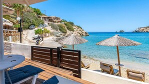 Een houten terras met lounge fauteuils en parasols met uitzicht op een heldere blauwe zee, met gebouwen en groen op de achtergrond.