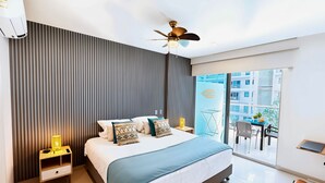 Ein modernes Hotelzimmer mit einem großen Bett, einem Deckenventilator, einem Balkon mit Tisch und Stühlen und Blick auf die Stadt.