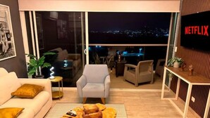 A modern living room with a sofa, armchair, coffee table, and a TV screen displaying the Netflix logo.