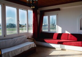 A room with a white sofa, a red sofa, and a window seat overlooking a green landscape.