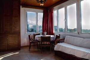 Una habitación acogedora con una mesa de comedor, sillas y un sofá. Cuenta con ventanas amplias con cortinas y vistas al exterior.