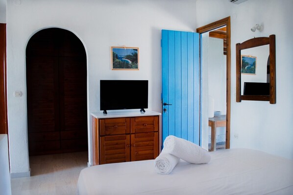 Une chambre avec une armoire en bois, un téléviseur posé sur une commode, une porte bleue et un lit avec une serviette enroulée.
