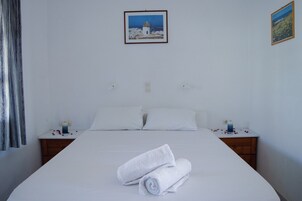 A hotel room with a neatly made bed, white linens, two bedside tables with candles, and a framed picture on the wall.