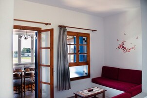 A room with a red sofa, a dining table with chairs, and a window with curtains.