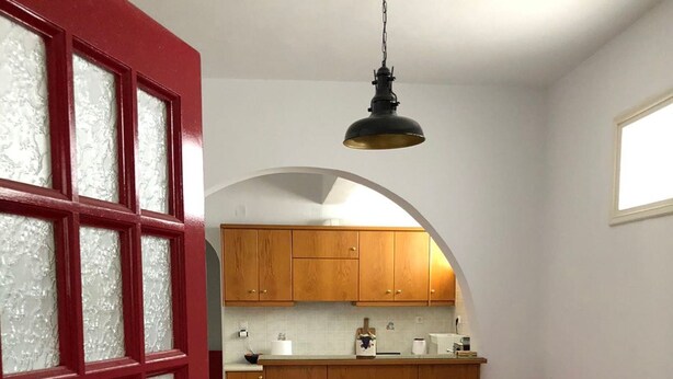 Una cocina compacta con armarios de madera, una mesa de comedor con sillas rojas y un sofá negro.
