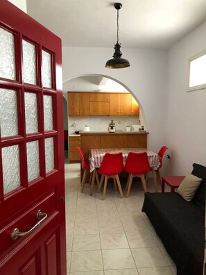A compact kitchen with wooden cabinets, a dining table with red chairs, and a black sofa.